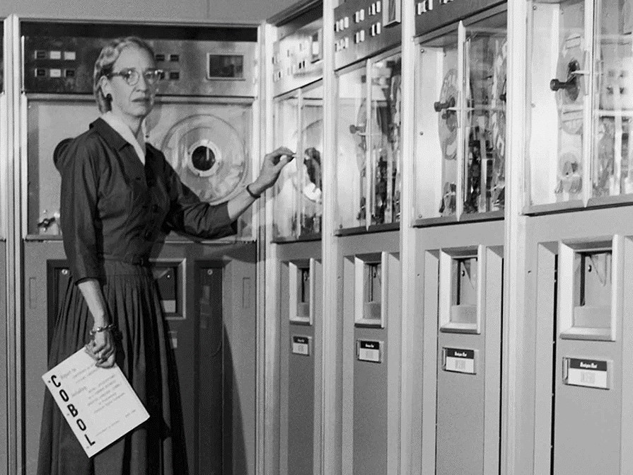 Grace Hopper ao lado de um computador